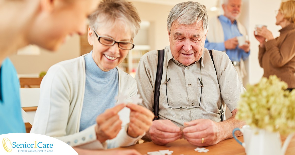 An older couple works on a puzzle with a caregiver, representing the kind of activity that helps those with dementia and also representing Alzheimer’s and Brain Awareness Month.