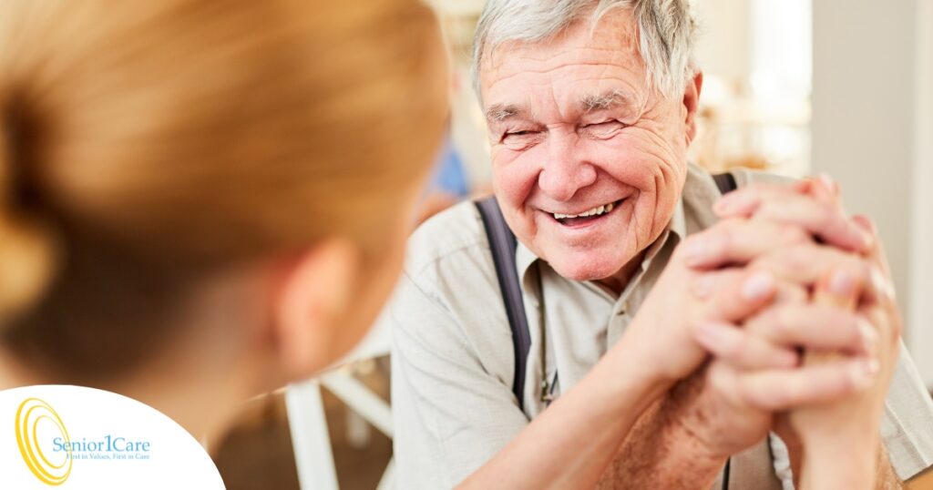 A caregiver holds hands with a happy older client, representing the results of creating a comfortable environment in the home.