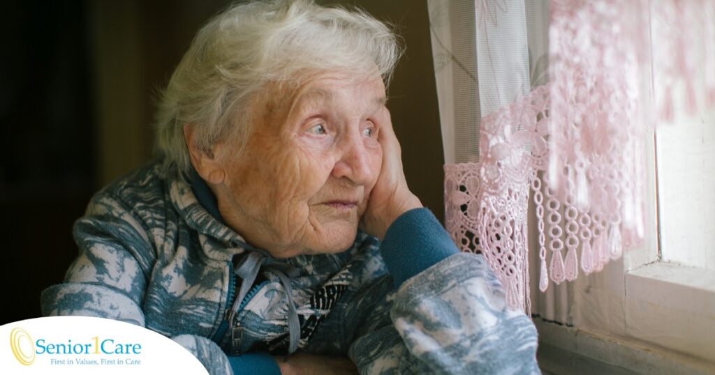 An older woman peacefully looks out of the window while the sun is still up, representing what can happen with sundowning.